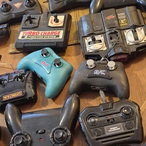 Pu&ograve; includere: Una collezione di vari telecomandi per auto RC neri e verde acqua. Alcuni telecomandi hanno il testo "Turbo Charge 6 Function System" e "New Bright". Altri telecomandi hanno il testo "R/C".