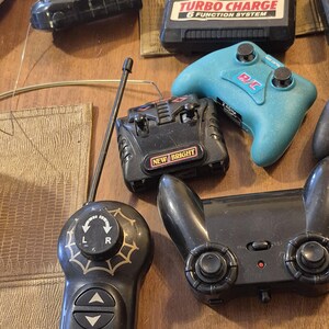 Pu&ograve; includere: Una collezione di telecomandi vintage di varie forme e dimensioni. I telecomandi sono principalmente neri, con alcuni dettagli rossi, bianchi e blu. &Egrave; visibile anche un controller turchese. I telecomandi hanno pulsanti, joystick e antenne.