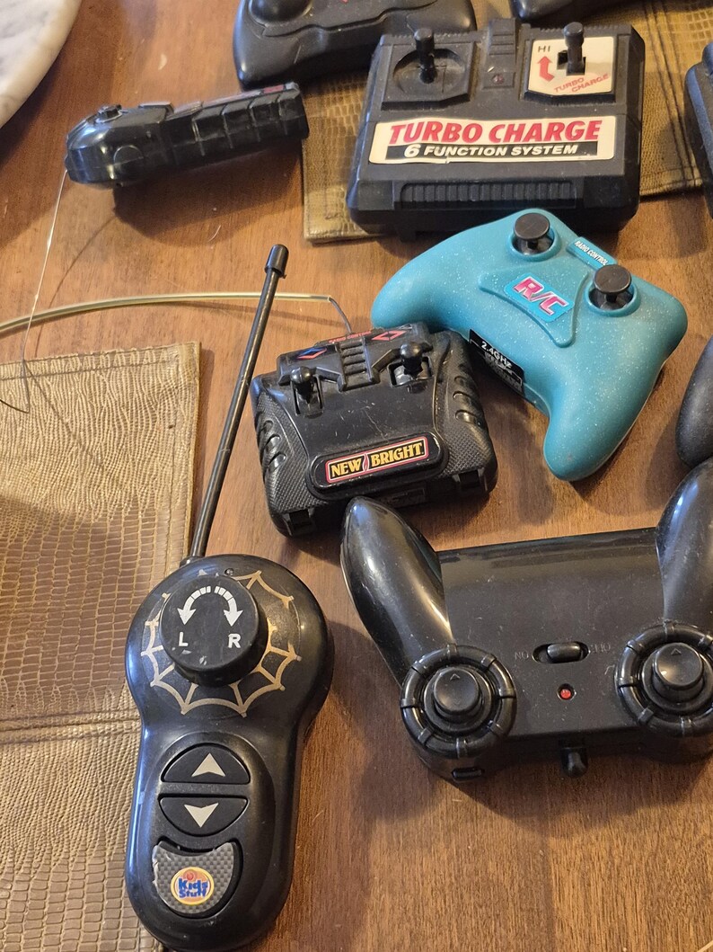 Pu&ograve; includere: Una collezione di telecomandi vintage di varie forme e dimensioni. I telecomandi sono principalmente neri, con alcuni dettagli rossi, bianchi e blu. &Egrave; visibile anche un controller turchese. I telecomandi hanno pulsanti, joystick e antenne.