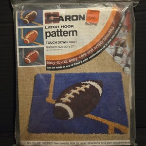May include: A sealed plastic package containing a latch hook pattern. The pattern features a football design with the text "TOUCH DOWN #3037". Finished size is 20" x 27". The package includes the text "easy-to-do, easy-care and simply beautiful".