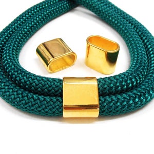 May include: A teal rope necklace with gold-coloured rectangular and oval clasps. The necklace is made of a thick, braided rope material. The clasps are shiny and metallic, providing a contrast to the matte texture of the rope.