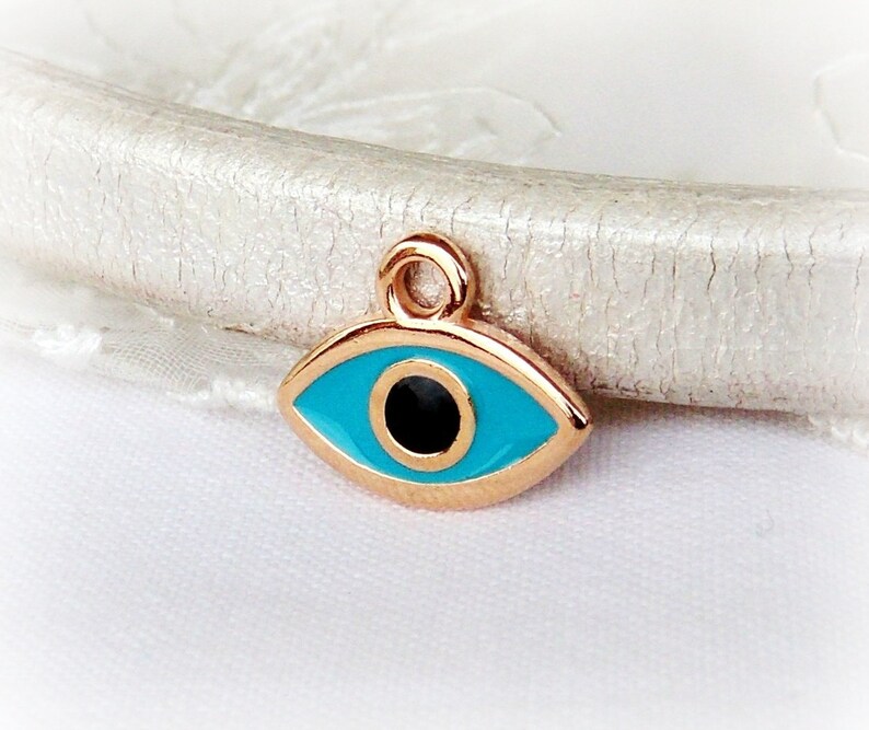 Puede incluir: Encanto de tono dorado con un dise&ntilde;o de ojo azul malvado. El ojo est&aacute; rodeado por un borde de tono dorado y tiene una pupila negra.
