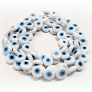 Può includere: Una collana di perline in ceramica bianca con disegni di occhi blu maligni.