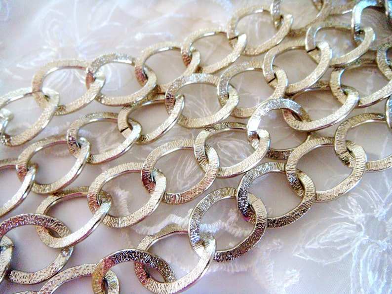 May include: A close-up of a silver chain with oval links. The chain is textured and has a shiny finish.