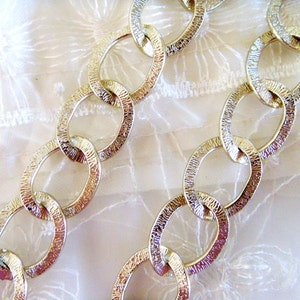 May include: A gold chain with textured oval links. The chain is lying on a white fabric background.