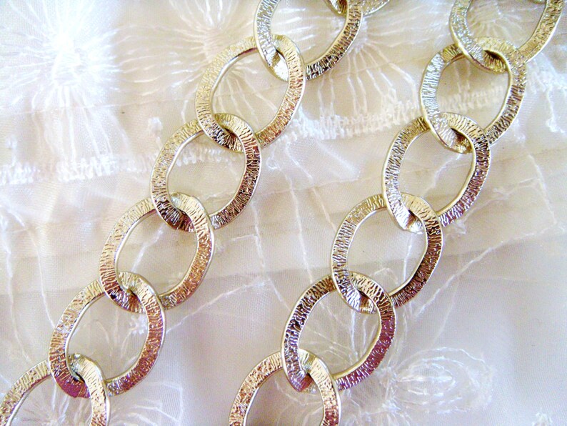 May include: A gold chain with textured oval links. The chain is lying on a white fabric background.