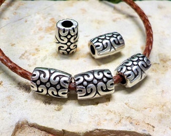 May include: Five silver metal beads with an intricate swirl design, strung on a brown leather cord. The beads are cylindrical and have a hole in the centre for threading.
