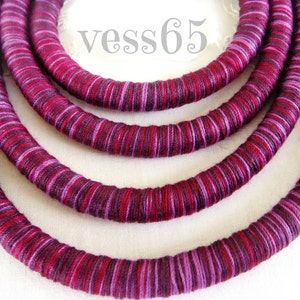 May include: Four strands of purple and pink striped cord, wrapped around each other, forming a circle. The cord is thick and textured, and the colors are vibrant.