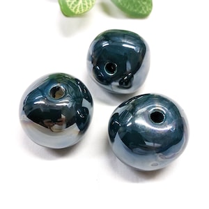Könnte beinhalten: Drei dunkelblaue Keramikperlen mit einem Loch in der Mitte. Die Perlen haben eine glänzende Oberfläche und sind rund.