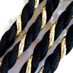 May include: Black braided cord with gold trim. The cord is twisted and has a shiny, metallic finish.