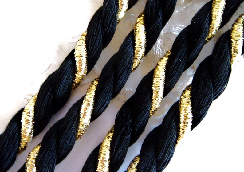 May include: Black braided cord with gold trim. The cord is twisted and has a shiny, metallic finish.