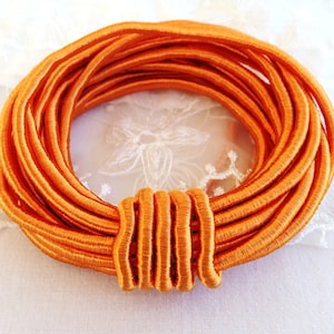 Könnte beinhalten: Nahaufnahme einer Spule mit orangefarbenem Gummiband. Das Band ist fest gewickelt und hat eine glatte, satinartige Oberfläche.