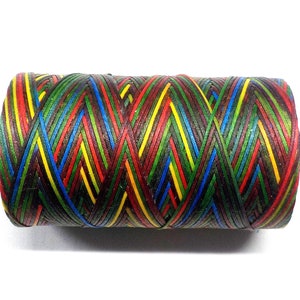 May include: A spool of colorful thread with a black background. The thread is woven in a diagonal pattern with red, yellow, green, and blue stripes.