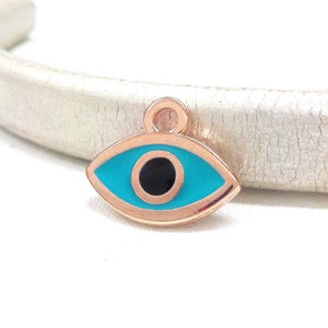 Puede incluir: Un amuleto de oro rosa en forma de ojo turco. El ojo es azul con una pupila negra y un contorno dorado.