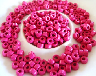Puede incluir: Primer plano de un plato blanco lleno de cuentas redondas de color rosa brillante. Las cuentas tienen un agujero en el centro y están dispuestas en un patrón circular.