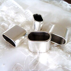 May include: Four silver-toned metal ring end caps, each with a smooth, rounded oval shape. The caps are arranged on a white fabric surface.