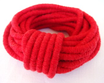 May include: A close-up of a red, coiled rope made of fabric. The rope is thick and has a soft, fuzzy texture.