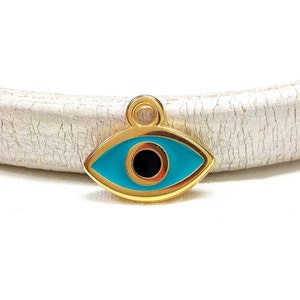 May include: Gold charm with a blue evil eye design. The eye is surrounded by a gold frame and has a black pupil.