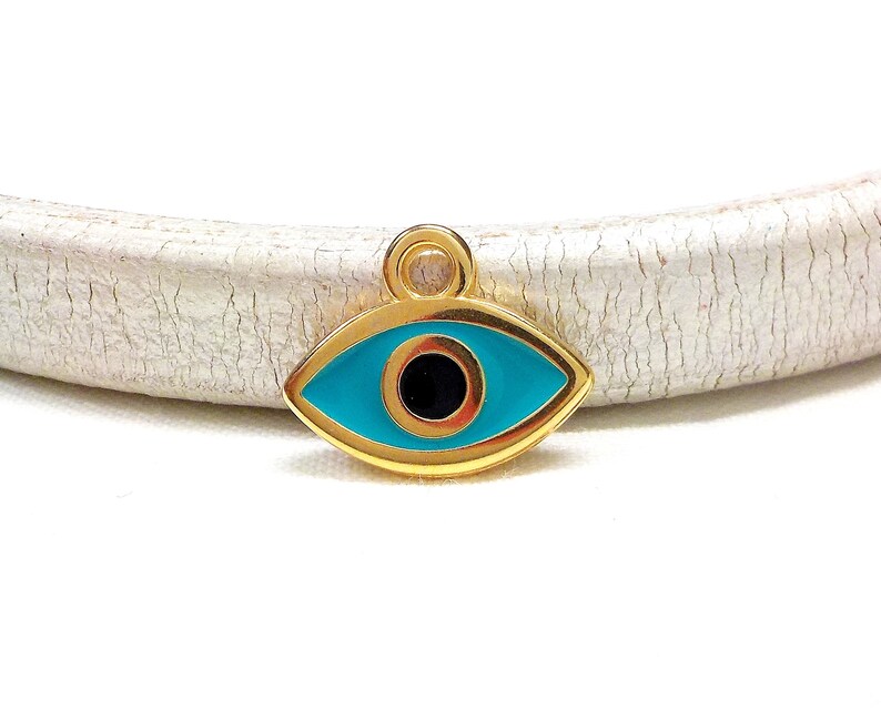 May include: Gold charm with a blue evil eye design. The eye is surrounded by a gold frame and has a black pupil.