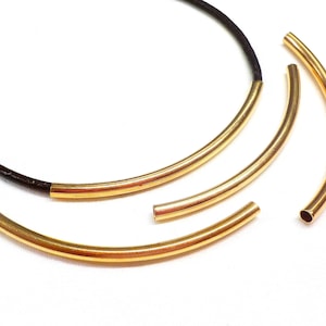 Pode incluir: Quatro aros de metal de cor dourada de tamanhos diferentes, com um cordão de couro preto preso ao aro maior.