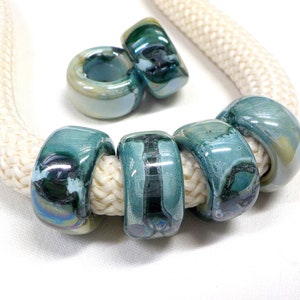 May include: A set of six teal and green glass beads with a white rope cord. The beads have a mottled, iridescent finish.
