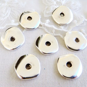 May include: Seven silver-toned metal beads with a hole in the center. The beads are irregularly shaped and have a smooth, shiny finish.