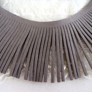 May include: A close-up of a brown suede fringe trim. The fringe is approximately 2.5 cm long and is arranged in a semi-circle.