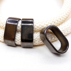 Puede incluir: Tres terminales de cordón de metal negro para una cuerda o un cordón. Dos son rectangulares y uno es ovalado.