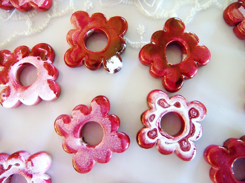 Puede incluir: Un conjunto de ocho cuentas de cer&aacute;mica de color rojo y blanco con forma de flor y un agujero en el centro. Las cuentas tienen un acabado brillante y son perfectas para hacer joyas o manualidades.