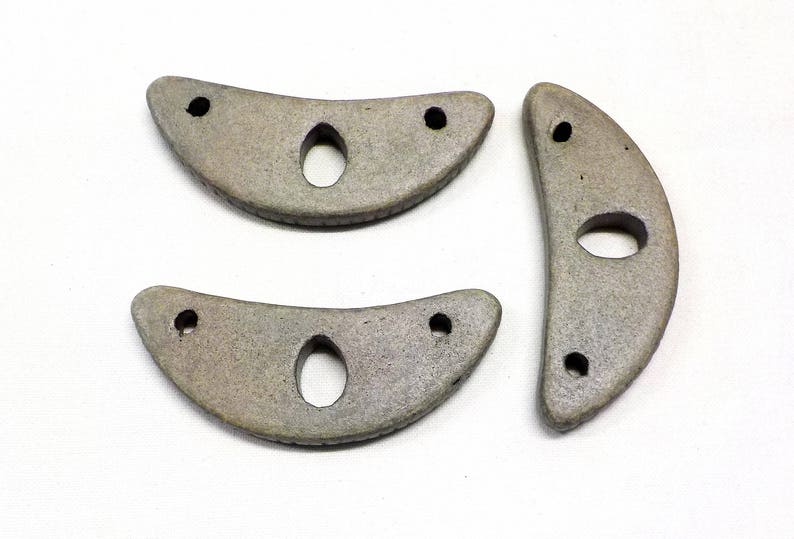 May include: Three gray ceramic crescent moon shapes with holes in the center. The shapes are slightly different sizes and have a rough texture.