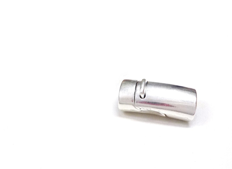 May include: A silver-colored magnetic clasp, designed for jewelry making. The clasp is cylindrical with a curved design and a small loop. It is shown against a white background.
