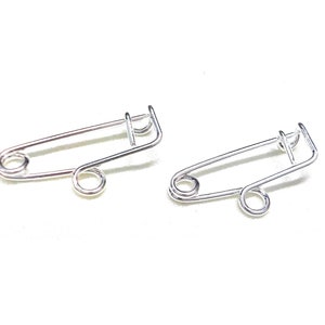 May include: Two silver safety pins, each with a spring-loaded clasp and a circular loop at the end.