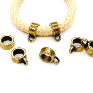 Pode incluir: Pontas de cordão de metal dourado antigo com um laço em cada extremidade. As pontas de cordão são projetadas para serem usadas com um cordão ou corda para criar joias ou outros artesanatos.