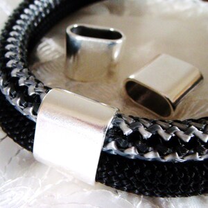 May include: Three silver metal cord end caps. The caps are oval shaped and have a smooth, shiny finish. The caps are on a black and white braided cord.