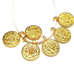 May include: A gold necklace with six round pendants featuring Chinese characters and intricate designs. The necklace is strung on a white cord.