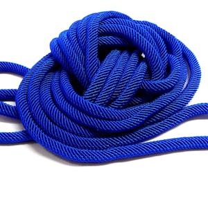 Op de afbeelding: Een opgerolde, helderblauwe touw. Het touw is strak opgerold en heeft een getextureerd oppervlak. De kleur is een diep, verzadigd blauw. De achtergrond is wit.