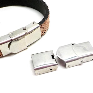 May include: Two silver metal clasps for a bracelet. One clasp is closed and the other is open. The clasps are designed to be used with a leather bracelet.