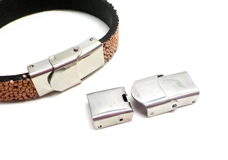 May include: Two silver metal clasps for a bracelet. One clasp is closed and the other is open. The clasps are designed to be used with a leather bracelet.