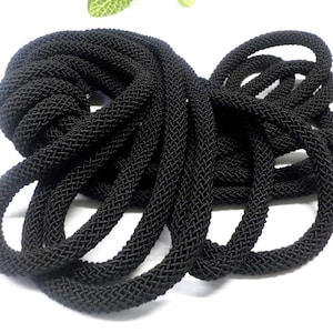 May include: Black braided cord, a thick, flexible rope with a woven texture. It is coiled and arranged in a pile.