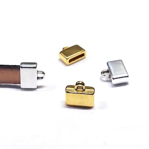 Könnte beinhalten: Drei Metall-Endkappen für Lederriemen. Zwei sind golden und eine ist silber. Die Endkappen sind rechteckig mit einer kleinen Schlaufe oben.