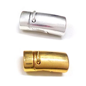 May include: Two magnetic clasps, one silver-colored and one gold-colored, are displayed against a white background. The clasps are cylindrical with a curved design and a small, curved metal piece on top.
