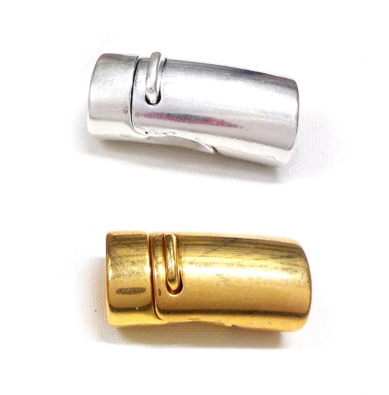 May include: Two magnetic clasps, one silver-colored and one gold-colored, are displayed against a white background. The clasps are cylindrical with a curved design and a small, curved metal piece on top.