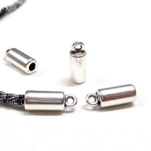 May include: Three silver metal cord end caps with a loop on one end. The caps are cylindrical and have a smooth, polished finish.