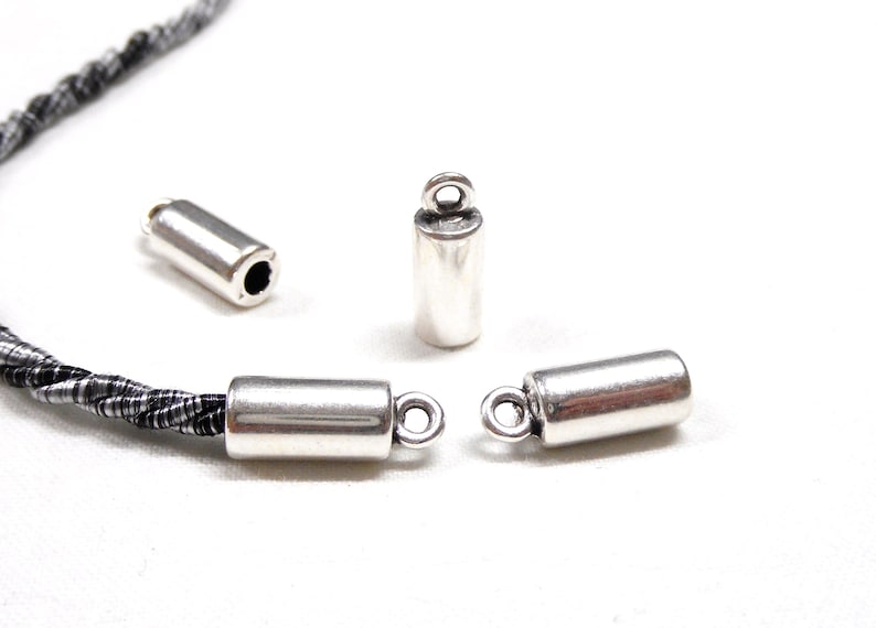 May include: Three silver metal cord end caps with a loop on one end. The caps are cylindrical and have a smooth, polished finish.