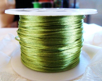 May include: A spool of green satin cord, wound around a white plastic spool. The cord is smooth and shiny.