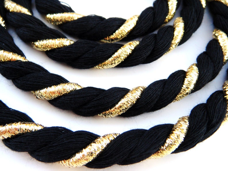 May include: Black and gold rope trim with a twisted design. The rope is black with a thin gold thread running through it.