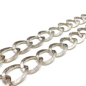 May include: A silver chain with oval links. The links have a textured surface.