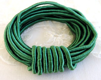 May include: A spool of emerald green elastic cord, wound into a circle. The cord is made of a soft, silky material and is perfect for crafting projects.