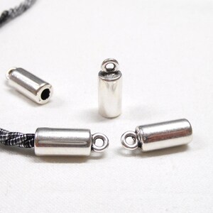 May include: Three silver metal cord end caps with a loop on one end. The caps are cylindrical and have a smooth, polished finish.