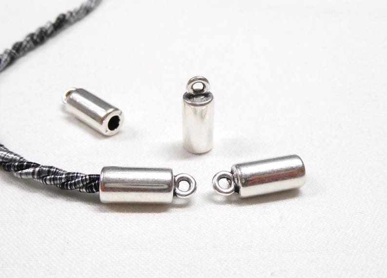 May include: Three silver metal cord end caps with a loop on one end. The caps are cylindrical and have a smooth, polished finish.